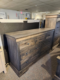 The Vokes 262-407 Bayshore 7 Drawer Dresser is displayed in a showroom among other furniture pieces.