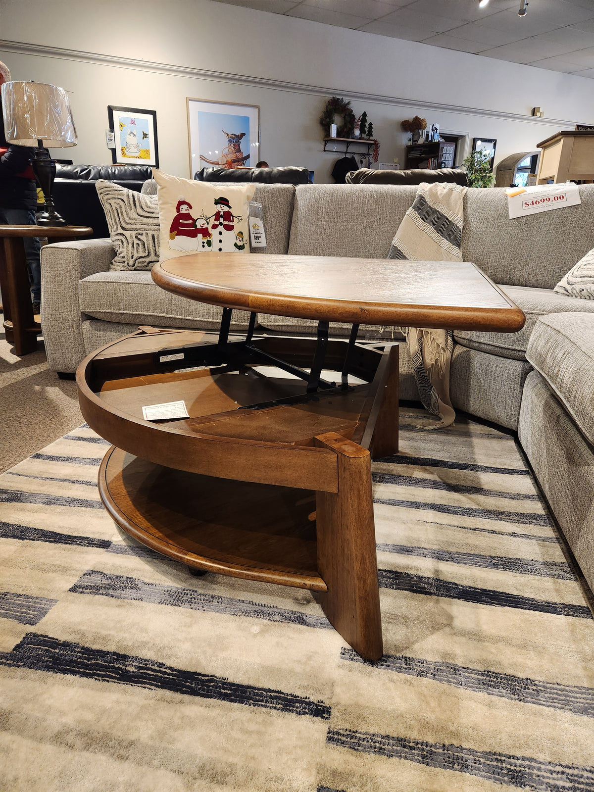 A Magnussen T6354 Tanner Pie Shape Lift Top Cocktail Table in Tawny Brown sits on a striped rug by casual sofas.