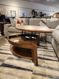 A Magnussen T6354 Tanner Pie Shape Lift Top Cocktail Table in Tawny Brown sits on a striped rug by casual sofas.