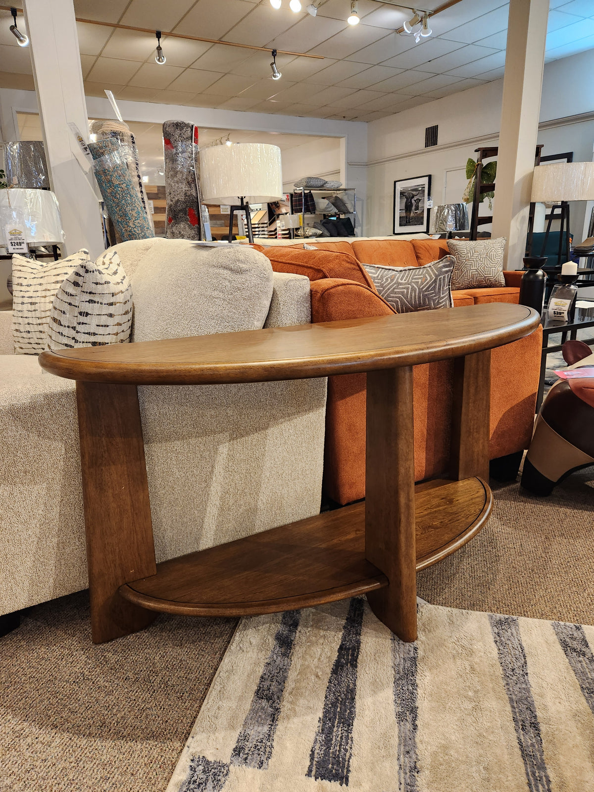 The Magnussen T6354 Tanner Demilune Sofa Table stands behind a beige sofa in the showroom.