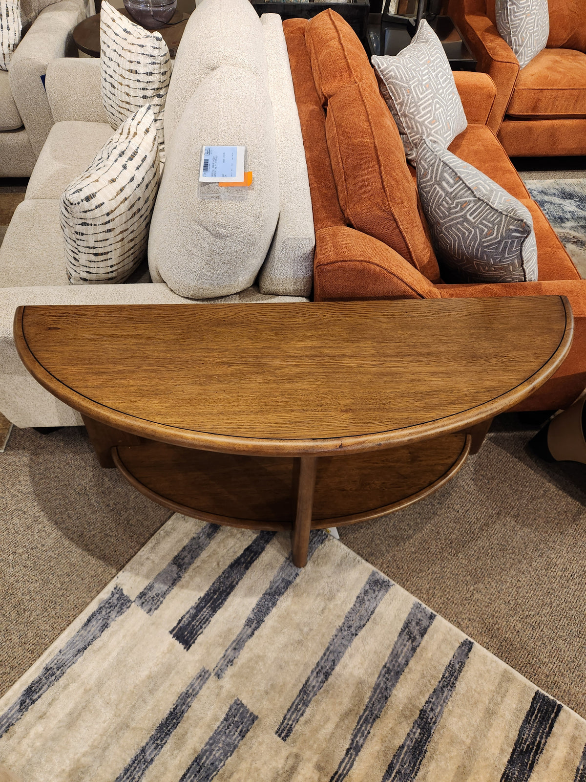 The Magnussen T6354 Tanner Demilune Sofa Table in Tawny Brown adds function between beige and orange couches.