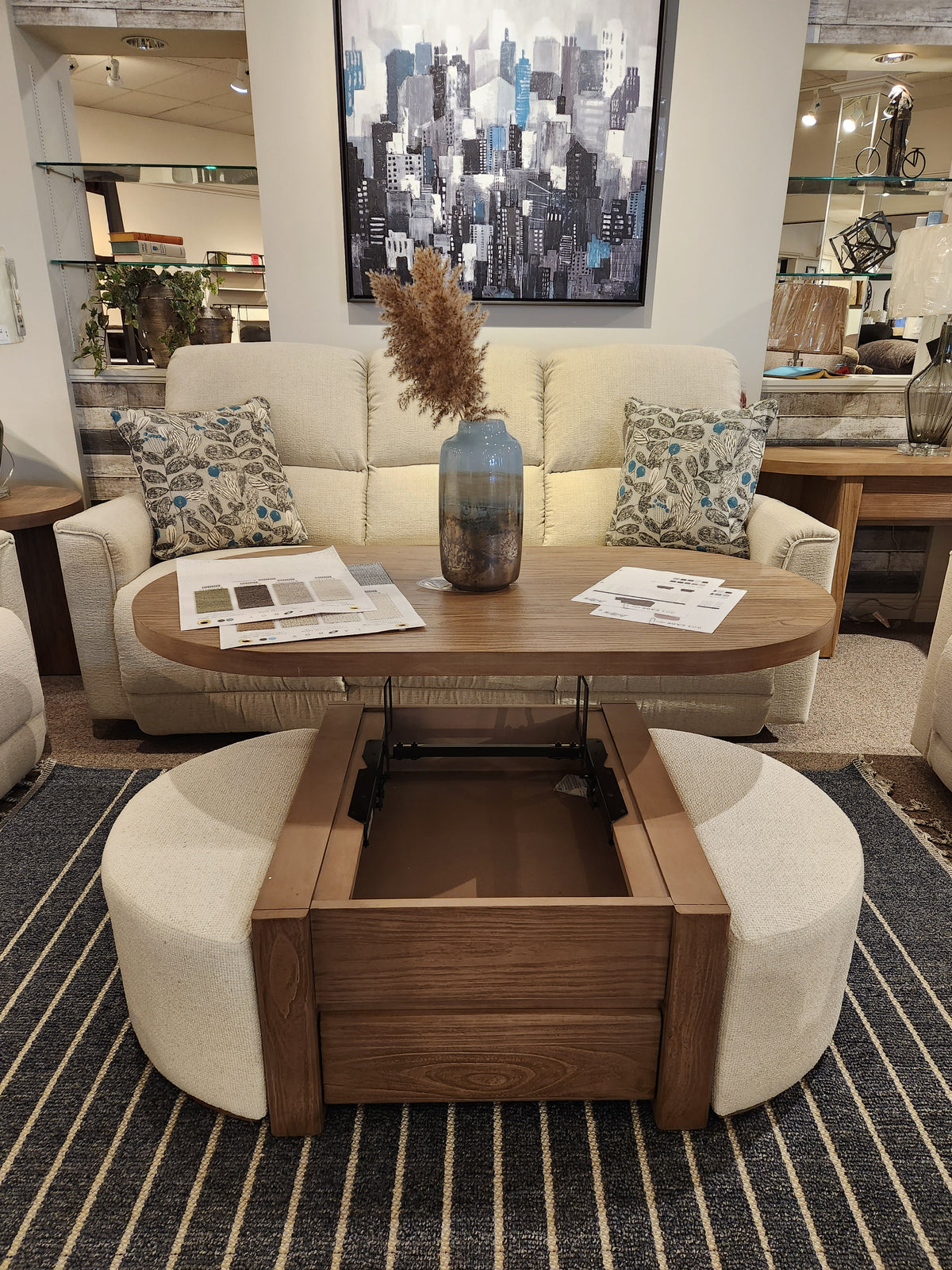 A Magnussen T6348 Hayden Lift Top Cocktail Table in Golden Oat, with storage, ottomans, and a beige sofa behind.