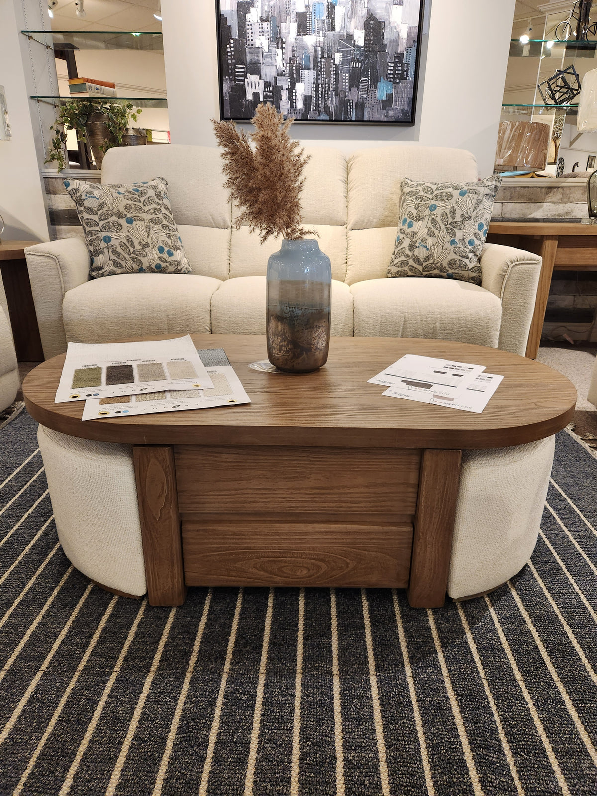 A beige sofa with patterned cushions sits behind a Magnussen T6348 Hayden Lift Top Cocktail Table on a striped rug.