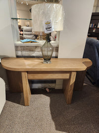 The Magnussen T6348 Hayden Sofa Table features a Golden Oat finish with natural wood textures, shown with a glass lamp.
