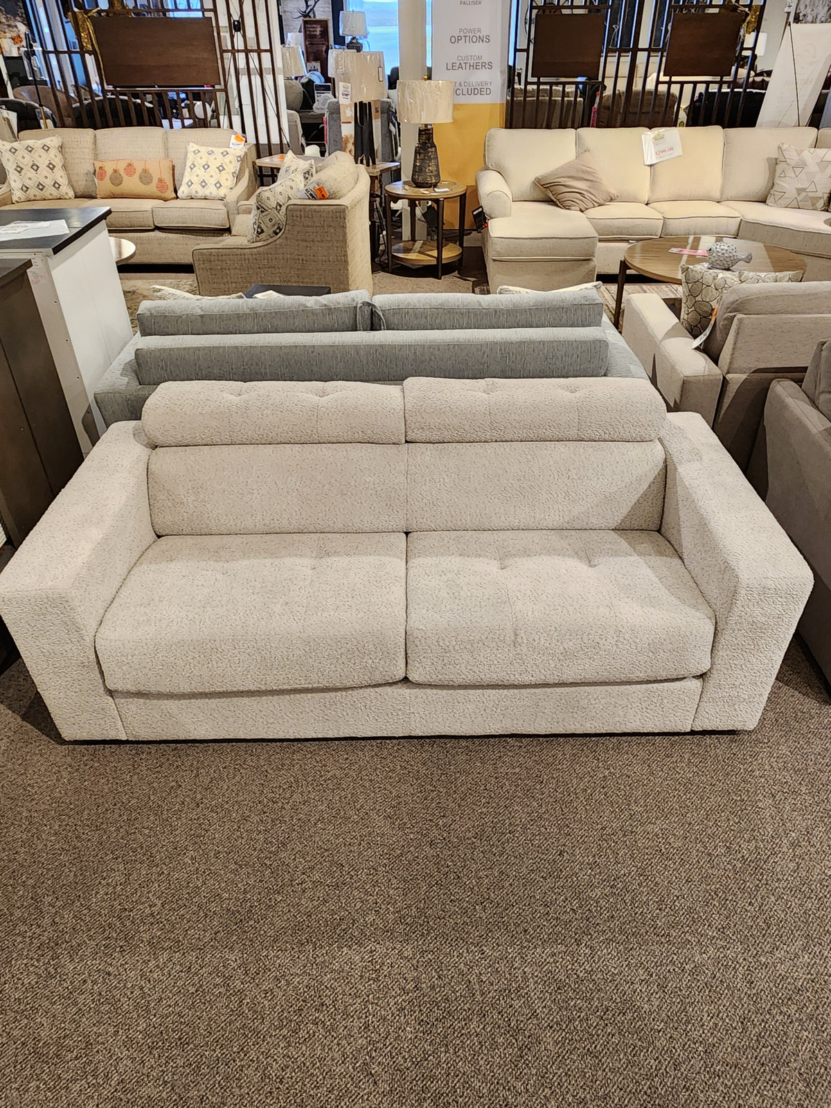 The Edison Queen Sofa Bed by Donald Choi, in light beige with wide armrests, is displayed among other sofas in a showroom.