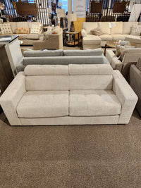 The Edison Queen Sofa Bed by Donald Choi, in light beige with wide armrests, is displayed among other sofas in a showroom.