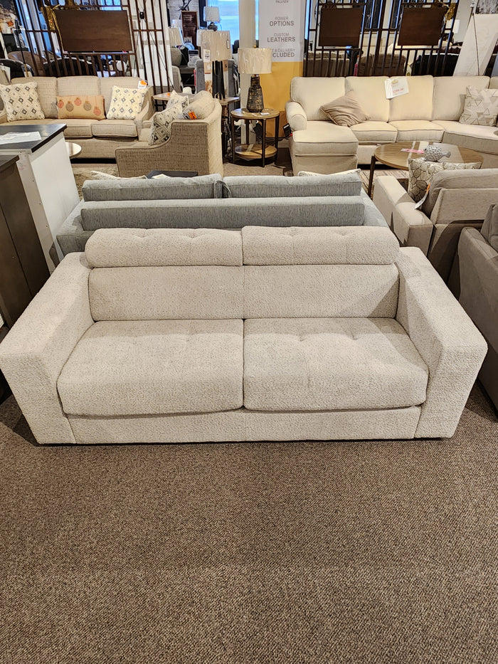 The Edison Queen Sofa Bed by Donald Choi, in light beige with wide armrests, is displayed among other sofas in a showroom.
