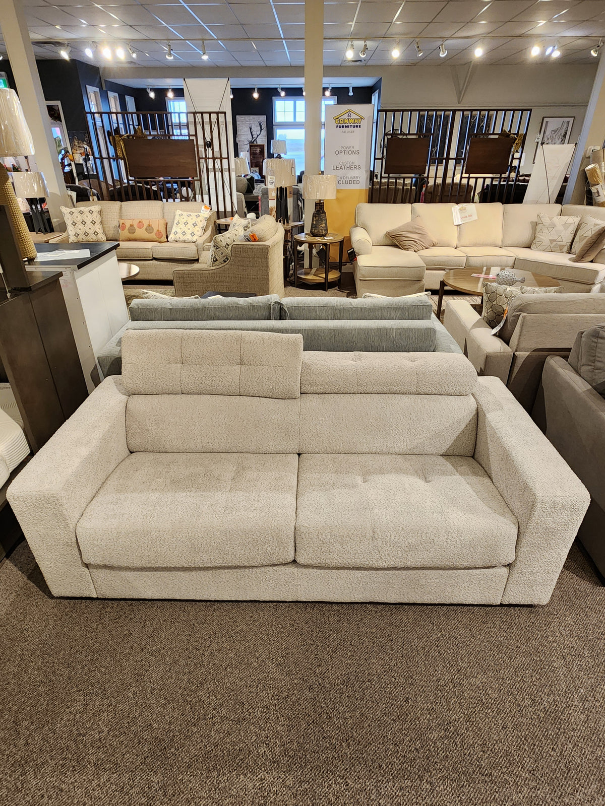 The Edison Queen Sofa Bed by Donald Choi in light beige with wide arms and hardwood frame is shown among other seating.