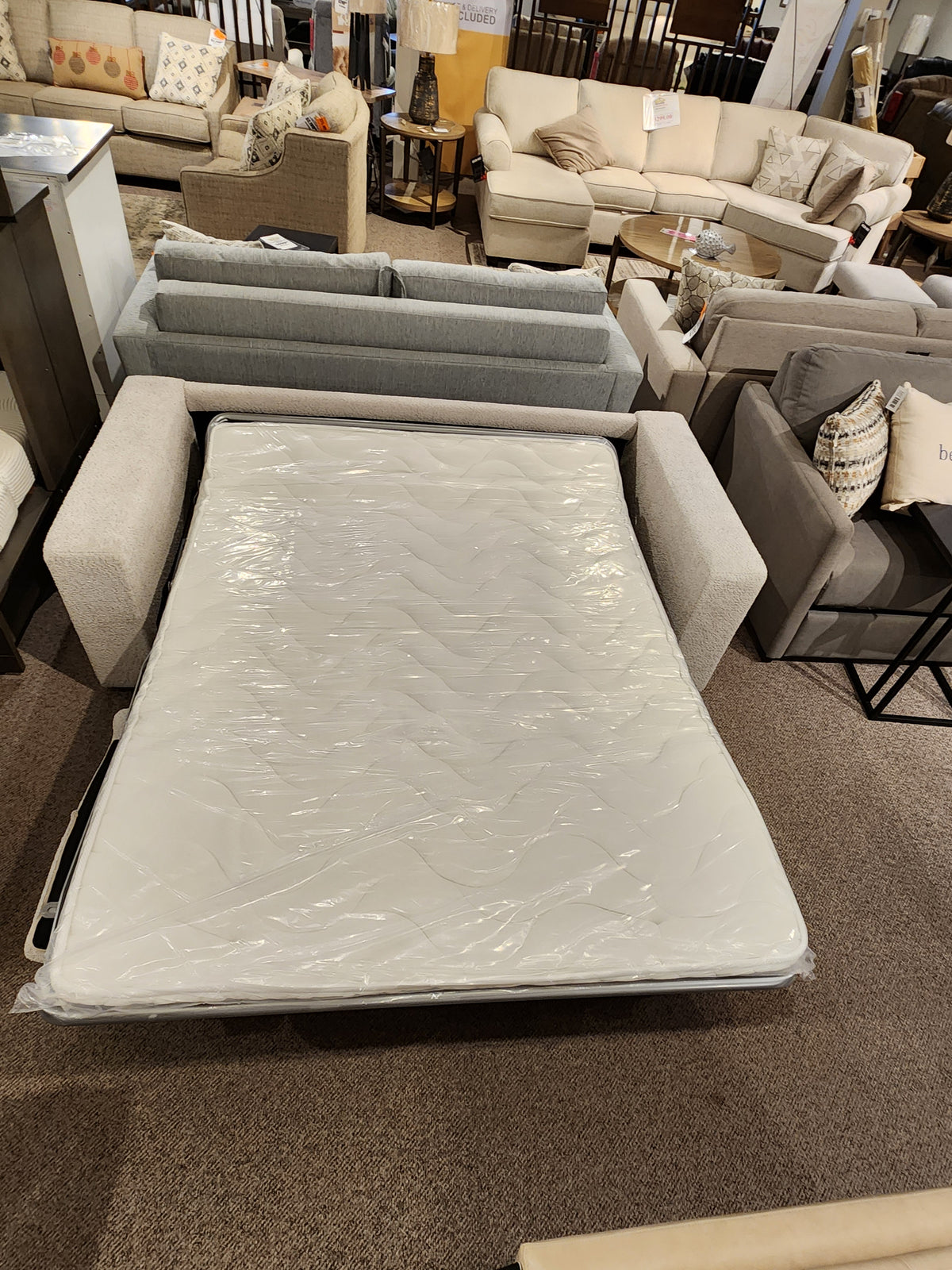 The Edison Queen Sofa Bed by Donald Choi, featuring a foam mattress in plastic, is displayed in a showroom.