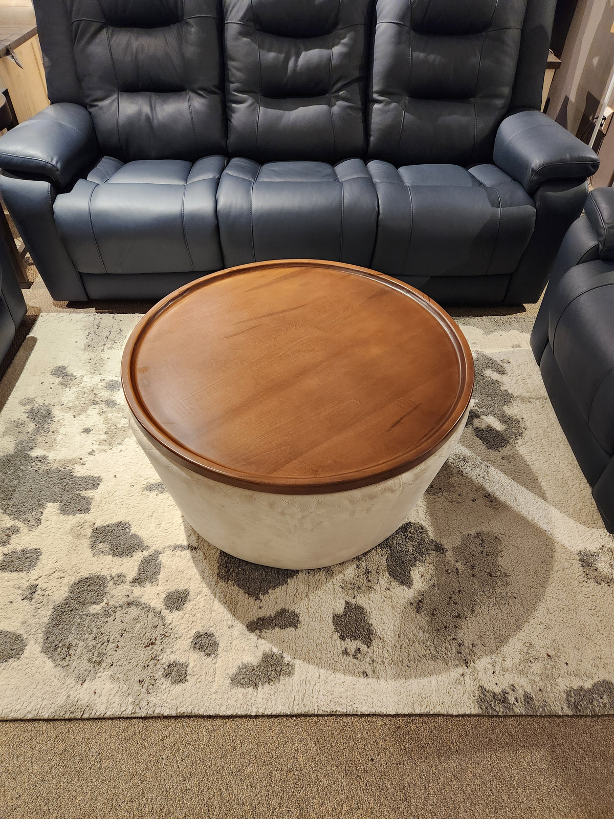 The 6415 Lift Top Storage Ottoman/Coffee Table by Decor-rest sits on a patterned rug, framed by dark blue leather sofas.