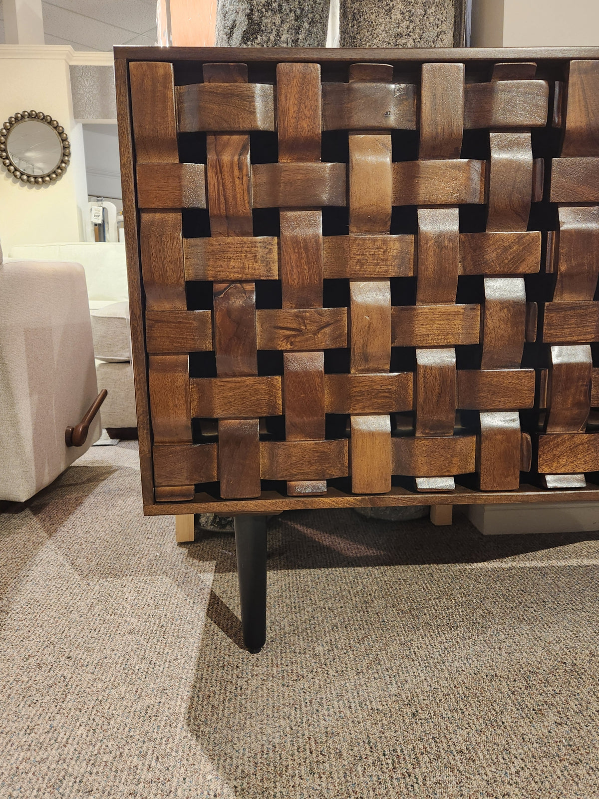 Close-up of Jofran's Trent Woven Front Accent Cabinet 60" with black tapered legs, crafted from mango wood, on carpet.