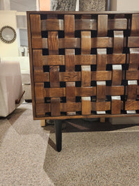 Close-up of Jofran's Trent Woven Front Accent Cabinet 60" with black tapered legs, crafted from mango wood, on carpet.