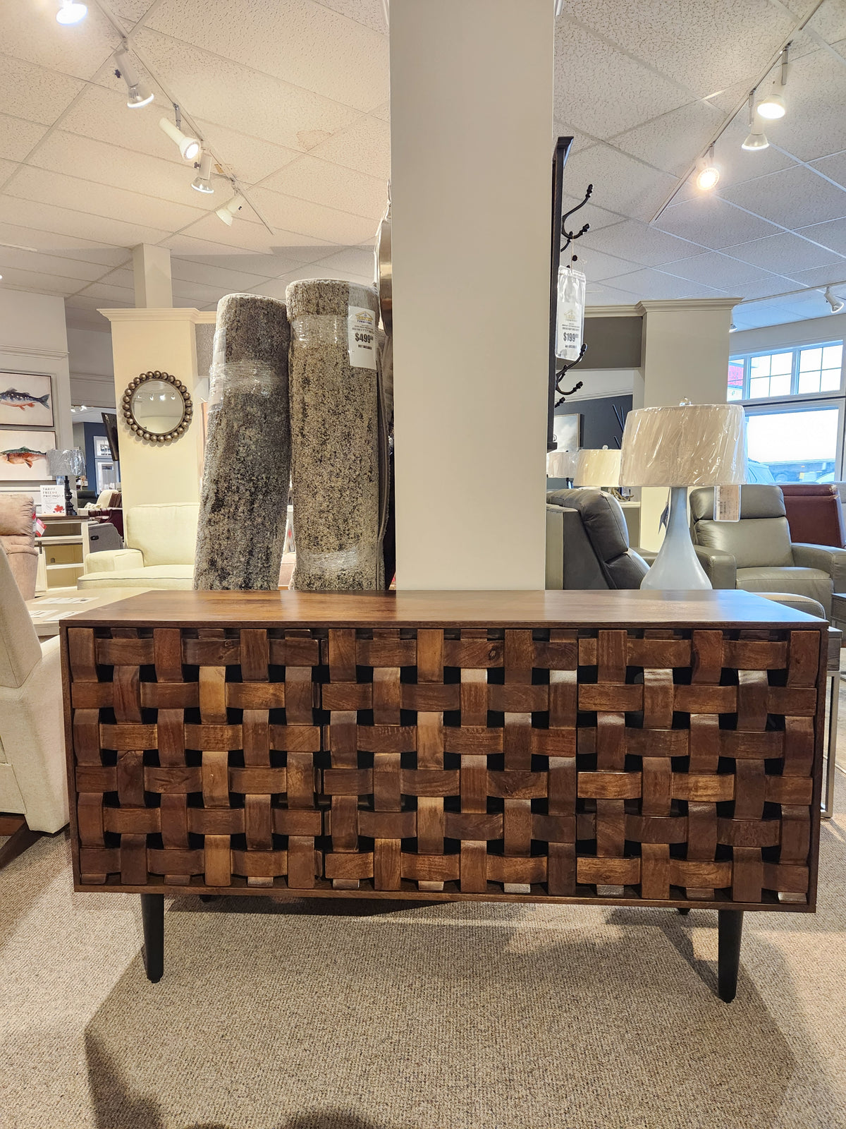 The Jofran Trent Woven Front Accent Cabinet 60" is shown in a showroom with lamps, rugs, and chairs in the background.