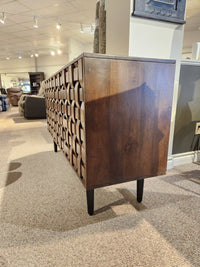 The Jofran Trent Woven Front Accent Cabinet 60" features a geometric design and black legs, shown on carpeted flooring.