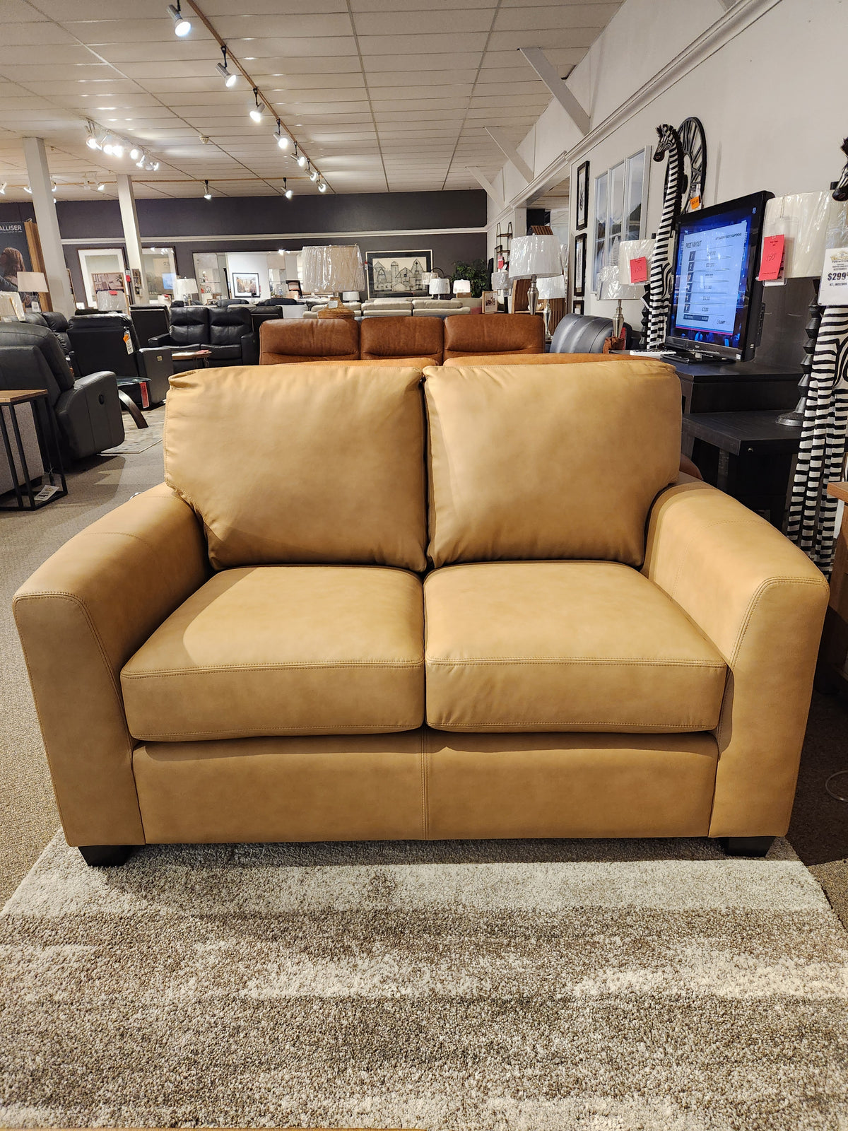 The Decor-rest 3968 Loveseat in tan leather with deep seats is displayed on a beige rug in a showroom.