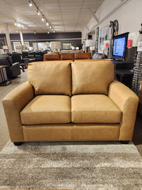 The Decor-rest 3968 Loveseat in tan leather with deep seats is displayed on a beige rug in a showroom.