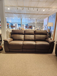 The Palliser 41051 Henry Sofa, a brown leather power recliner, is displayed in a carpeted showroom with overhead lights.