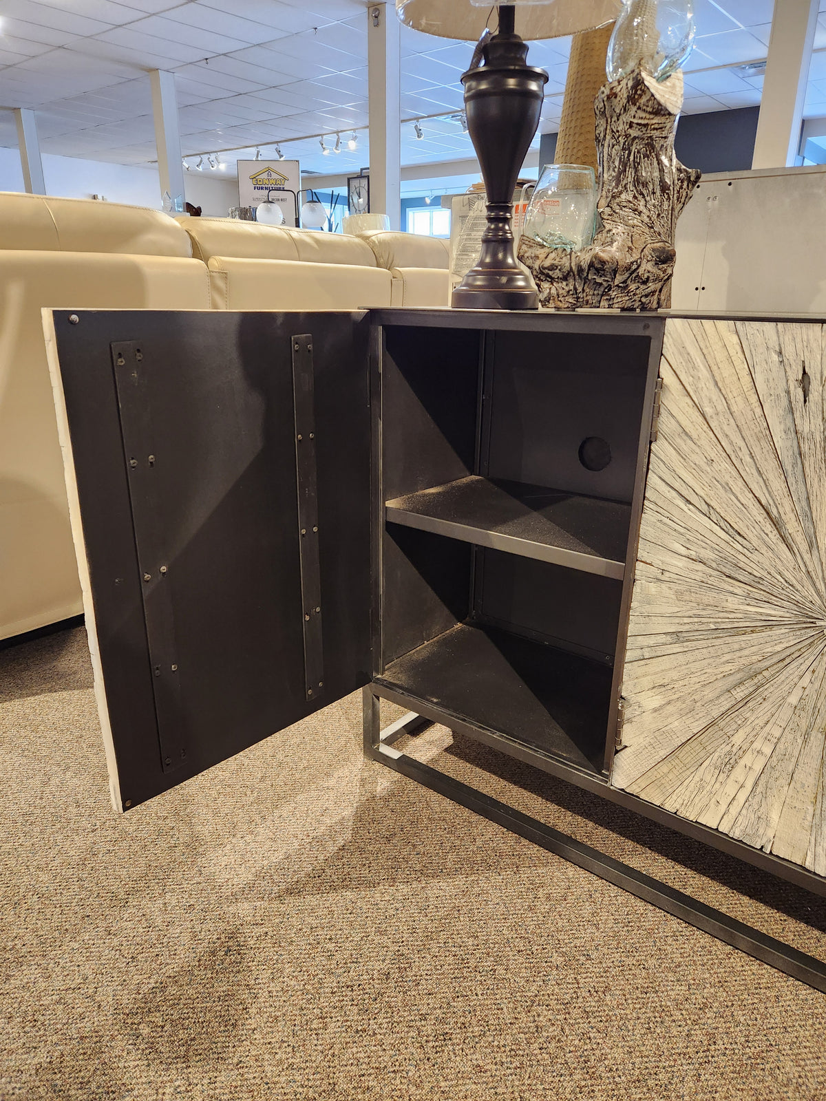 The Jofran 1929 Astral Plains 3 Door Cabinet has textured doors, black metal reveals, and two shelves on a carpeted floor.