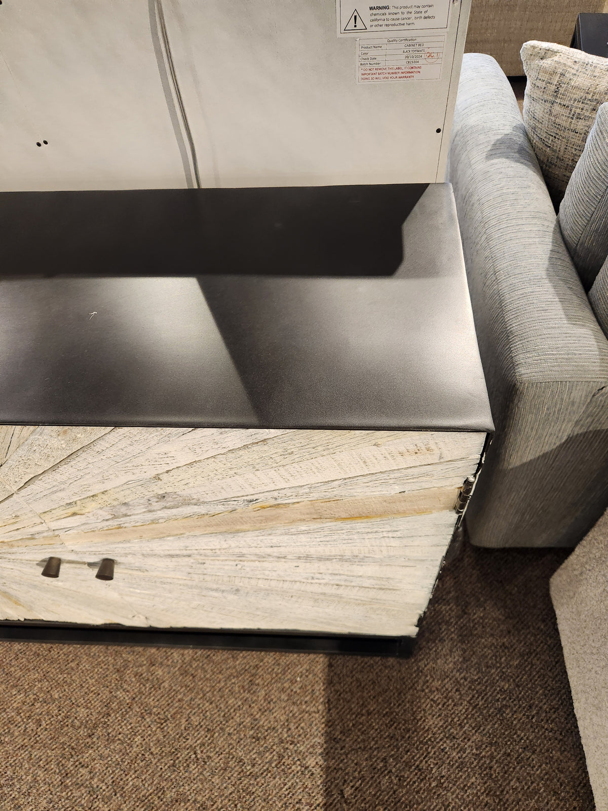 The Jofran 1929 Astral Plains 3 Door Cabinet stands by a light gray sofa on a brown carpeted floor.