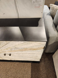 The Jofran 1929 Astral Plains 3 Door Cabinet stands by a light gray sofa on a brown carpeted floor.