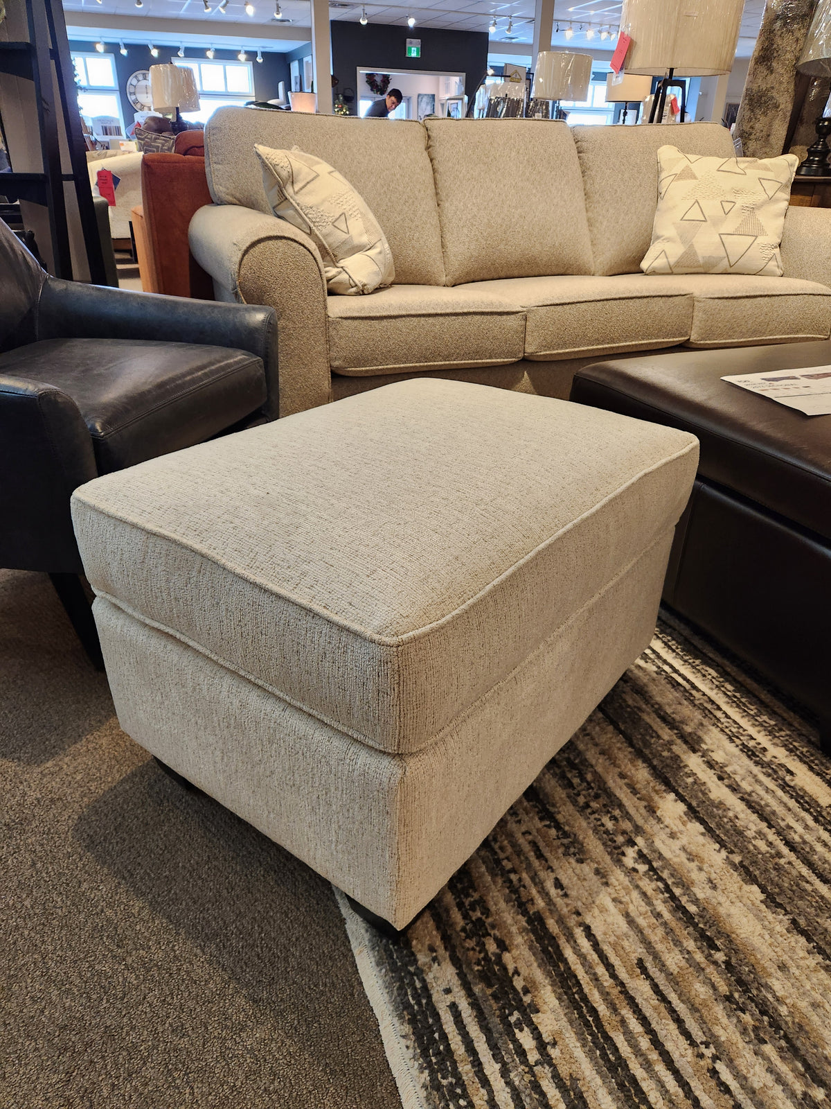 The Decor-rest 2541 Ottoman in beige adds extra seating or a cozy footrest in front of a matching showroom sofa.