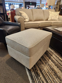 The Decor-rest 2541 Ottoman in beige adds extra seating or a cozy footrest in front of a matching showroom sofa.