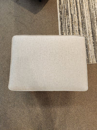 The Decor-rest 2541 Ottoman acts as a footrest or seat on a brown carpet beside a striped area rug, shown from above.