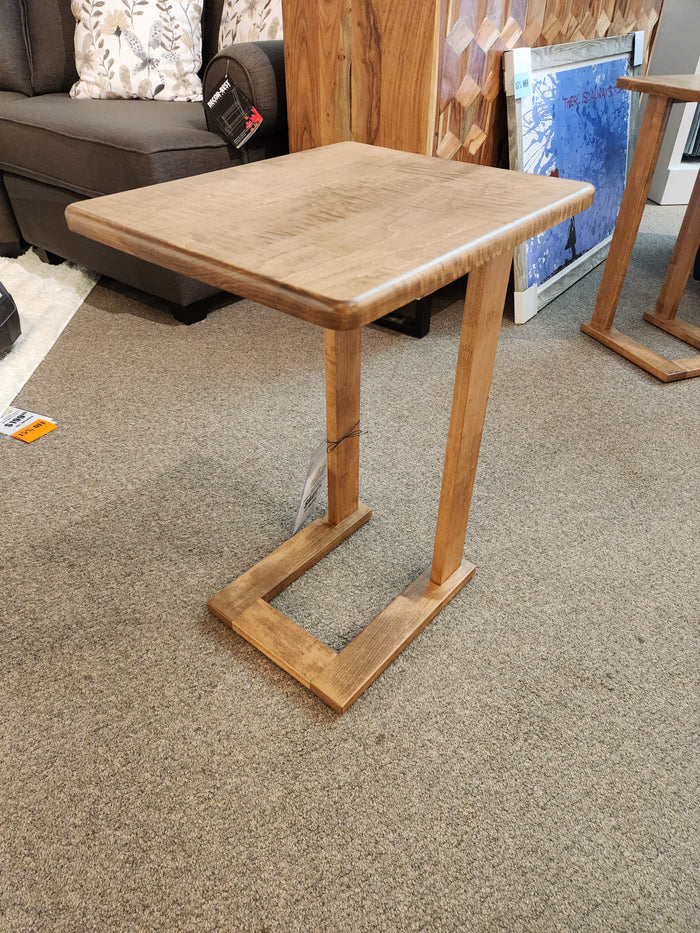 The Handstone AlaCarte Outback Snack Table, a small wooden C-shape, sits on carpet in a furniture store.