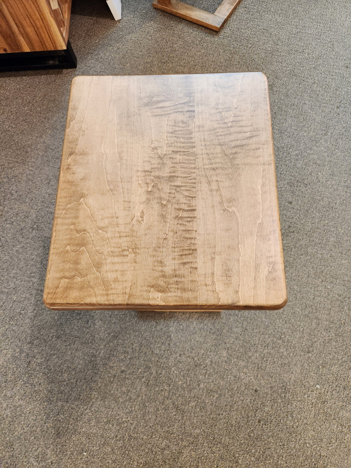The Handstone AlaCarte Outback Snack Table with a light brown finish sits on a gray carpeted floor.
