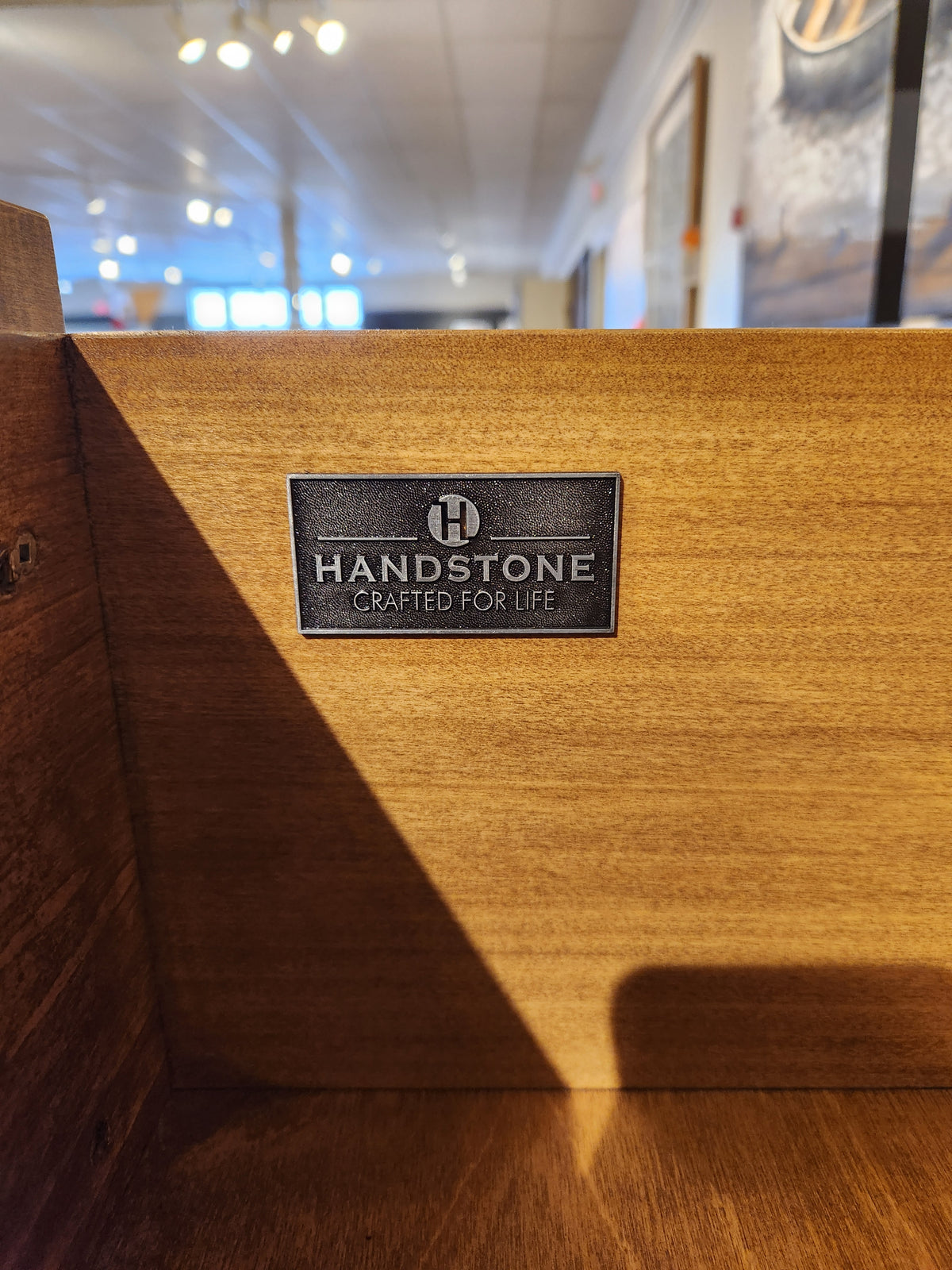 A metal plaque on the Glengarry HDTV Cabinet by Handstone displays the "Crafted for Life" logo.