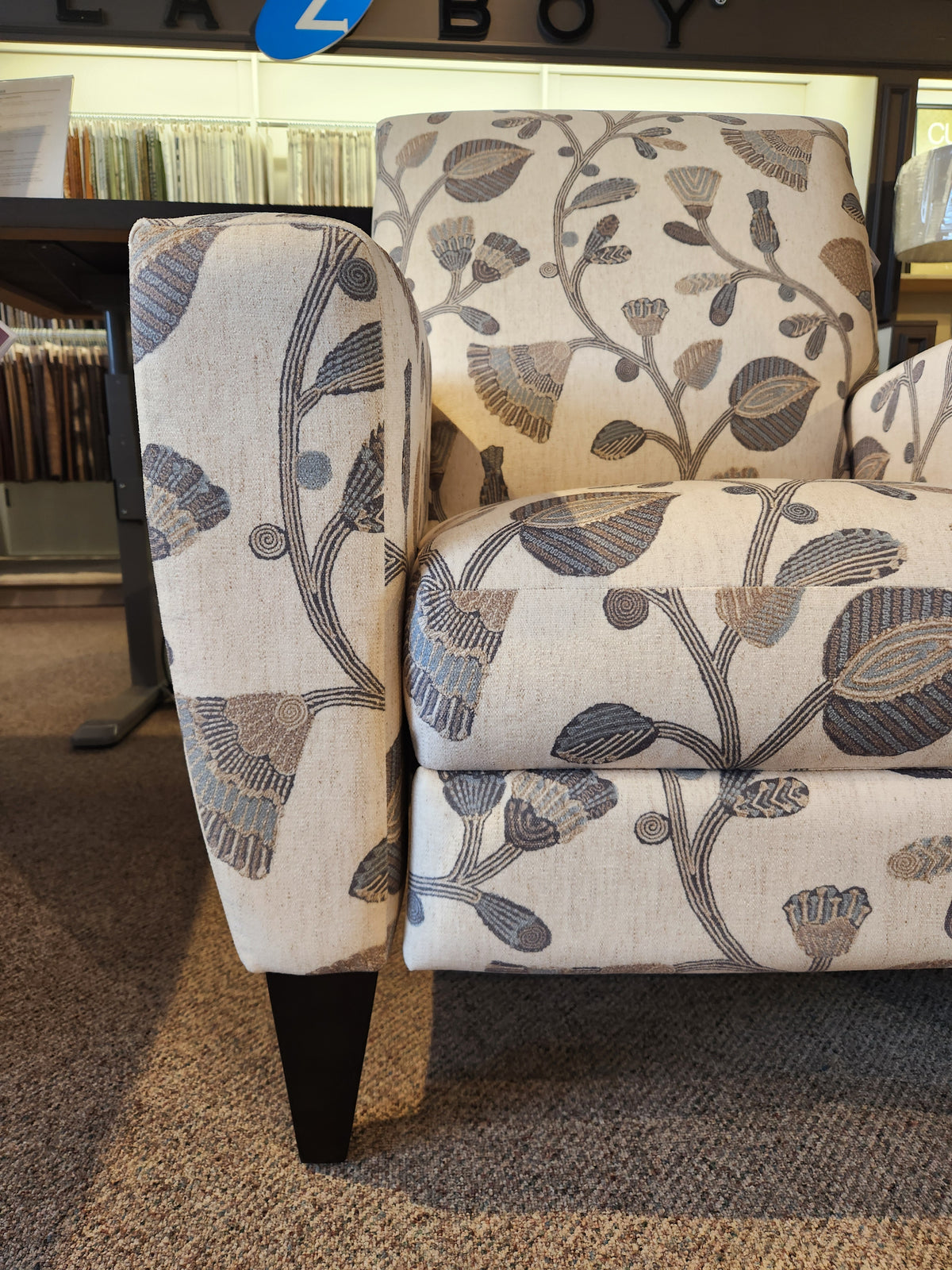 Close-up of La-z-boy 431 Scarlett High-Leg Recliner, a beige chair with gray floral pattern on display in store.