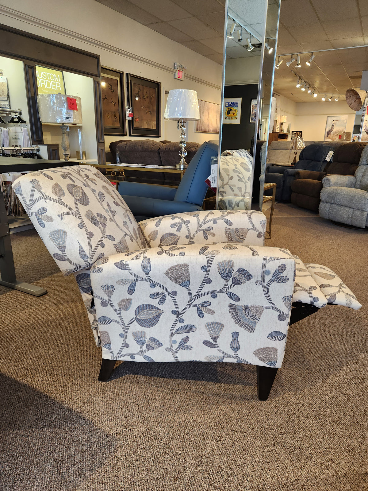 A La-z-boy 431 Scarlett High-Leg Recliner with floral pattern and extended footrest is displayed in the showroom.