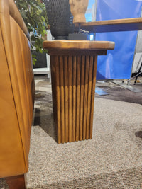 The Handstone Lotus Chairside Table with vertical slats sits by a tan leather sofa on a carpeted floor.