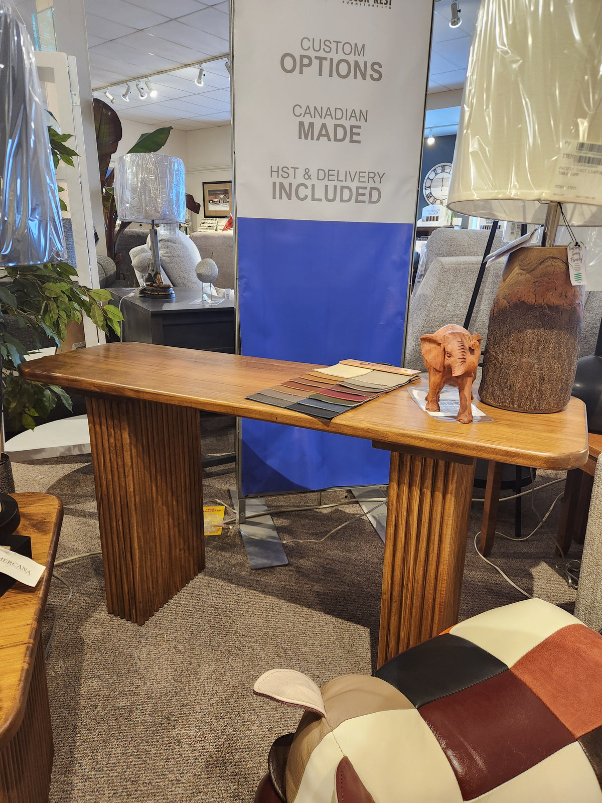The Handstone Lotus Sofa Table, shown with a small elephant figurine and color swatches in a furniture showroom.