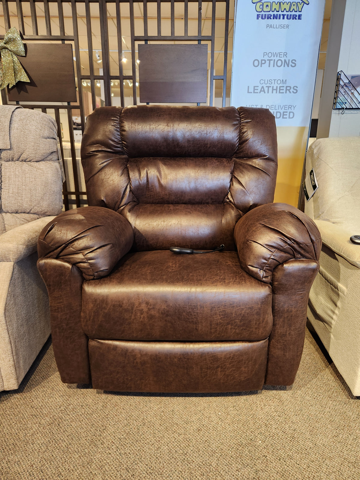 The Best 1B52 Troubadour Lift Chair is shown in a showroom, featuring brown leather and a remote on the seat.