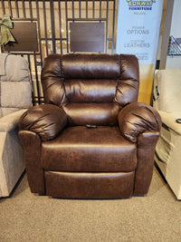 The Best 1B52 Troubadour Lift Chair is shown in a showroom, featuring brown leather and a remote on the seat.