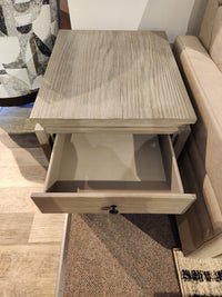 The Magnussen T5865 Conrad Rectangular End Table in Stone Harbor Grey sits between sofa and chair on carpet.