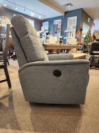 A gray Palliser 43003 Denali Swivel Power Glider is on display in a furniture store with tables and decor in back.