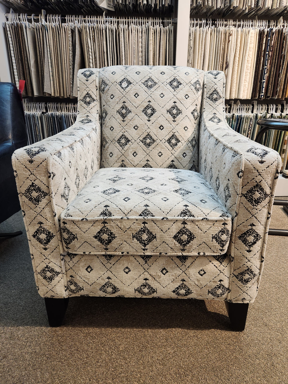 A Superstyle 828 Jasmine Chair with black and white geometric designs sits on a carpeted floor in a fabric showroom.