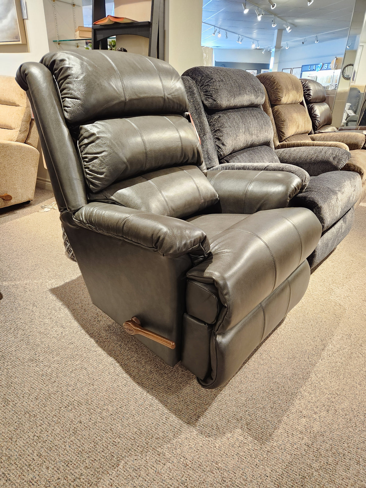 A La-z-boy 519 Astor Rocker Recliner in black is showcased in a showroom with other fabric recliners behind it.