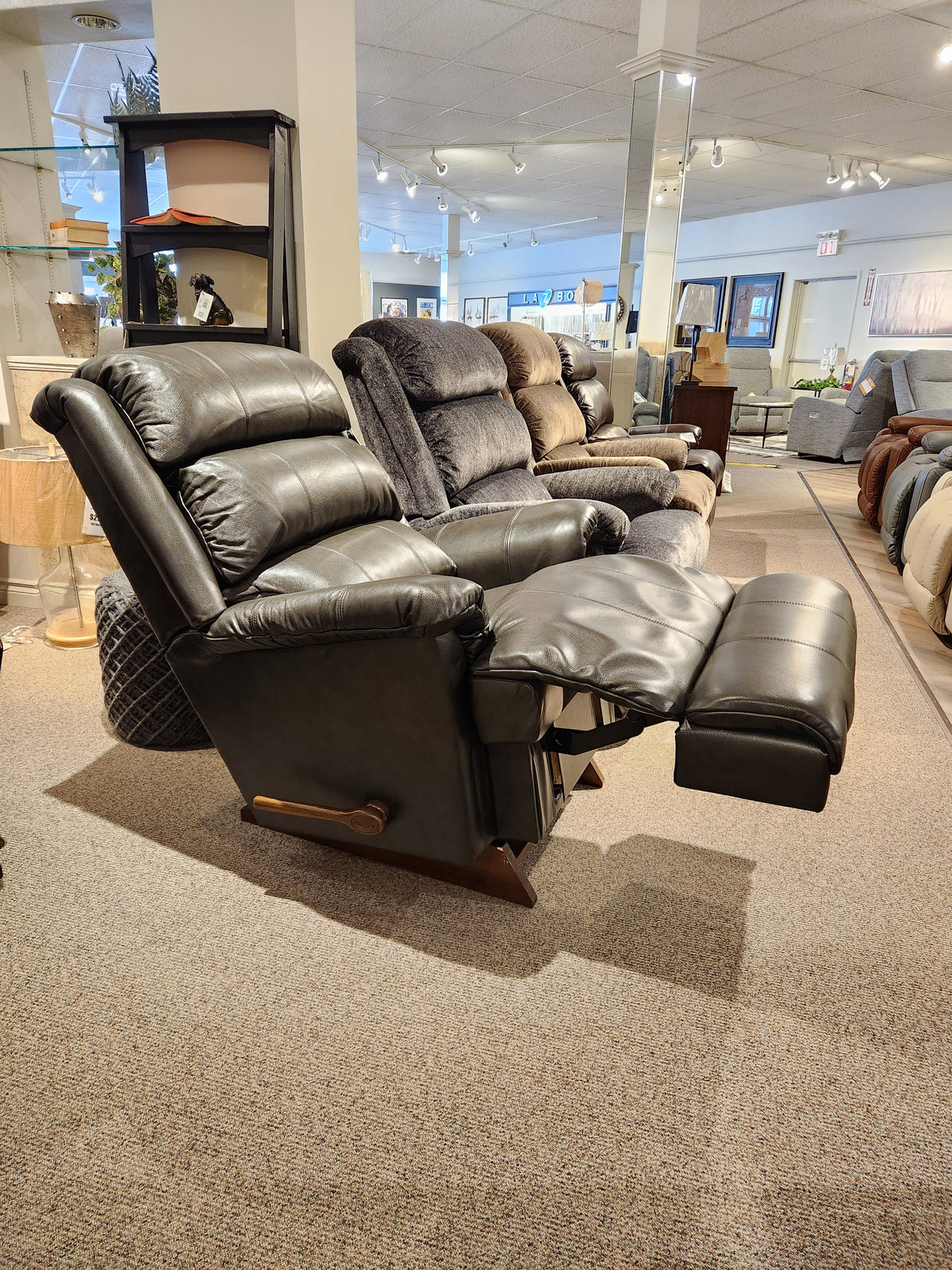 A row of recliners in a showroom, showcasing a fully extended La-z-boy 519 Astor Rocker Recliner in black leather.