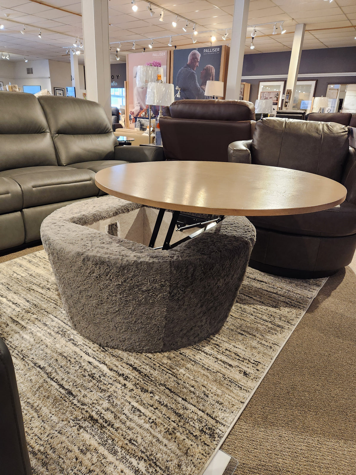 The Decor-rest 6415 Lift Top Storage Ottoman/Coffee Table is shown between leather sofas in the showroom.
