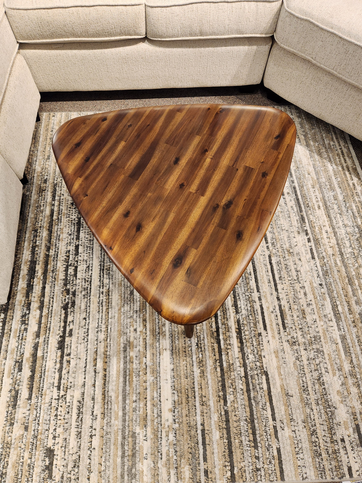 The 7110 Kacia Tri Coffee Table by Palliser sits on a patterned rug between sections of a beige sofa.