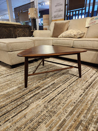 The 7110 Kacia Tri Coffee Table by Palliser sits on a striped rug before a beige sectional sofa in the showroom.