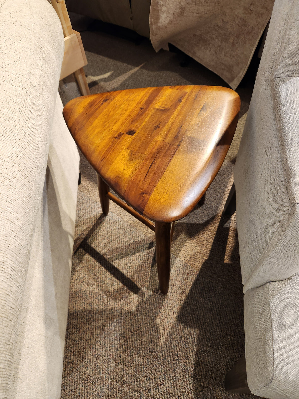 The Palliser 7110 Kacia Tri end Table sits between two beige sofas on a brown carpeted floor.