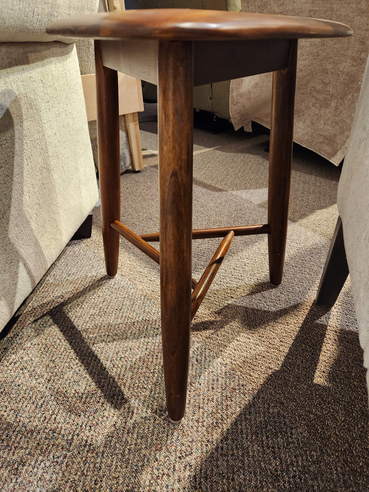 The Palliser 7110 Kacia Tri end Table, with three legs and triangular support, sits on a carpeted floor between chairs.