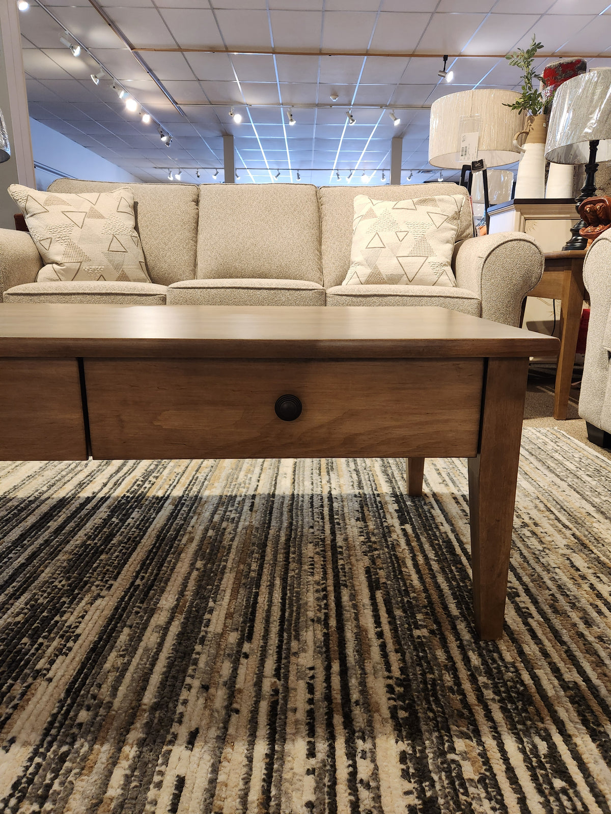 Durham 905-2 Drawer 48 x 24" Cocktail Table in Champagne sits before a beige sofa in a showroom.