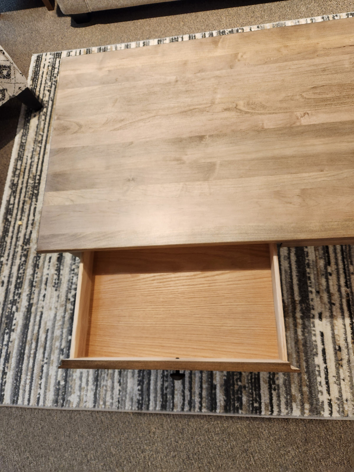 A Durham 905-2 drawer 48x24" cocktail table in Champagne sits on a patterned rug with an open empty drawer.