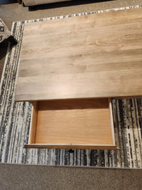 A Durham 905-2 drawer 48x24" cocktail table in Champagne sits on a patterned rug with an open empty drawer.