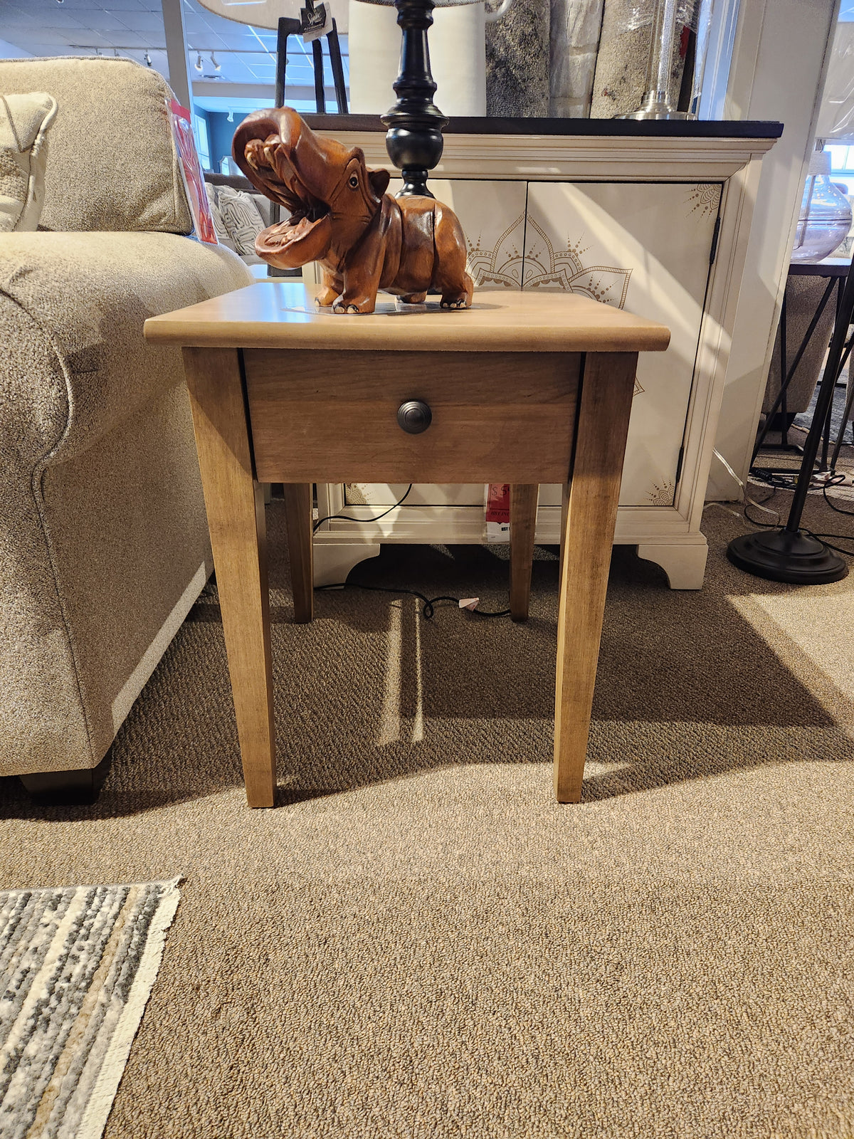 The Durham 905 20"x24" End Table in Champagne with drawer displays a carved hippo and black lamp on carpet.